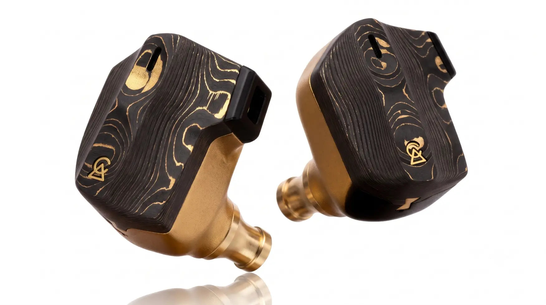 Angled close-up of Campfire Audio Solstice universal in-ear monitors with carbon fiber-brass damascus faceplates and matte gold PVD magnesium bodies, hand-built in Portland, Oregon.